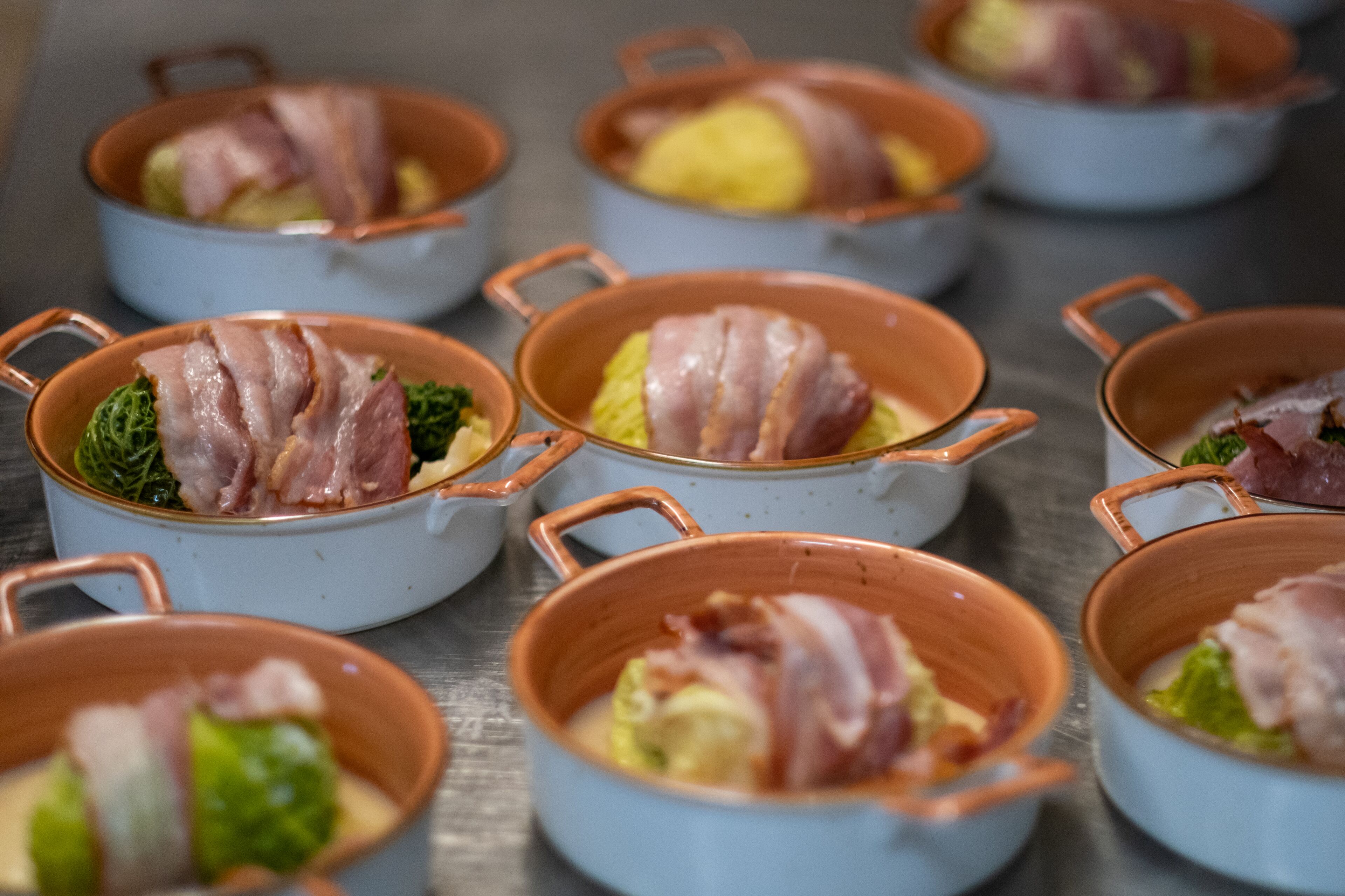 Multiple copper pots with handles, each containing food items and wrapped in bacon.
