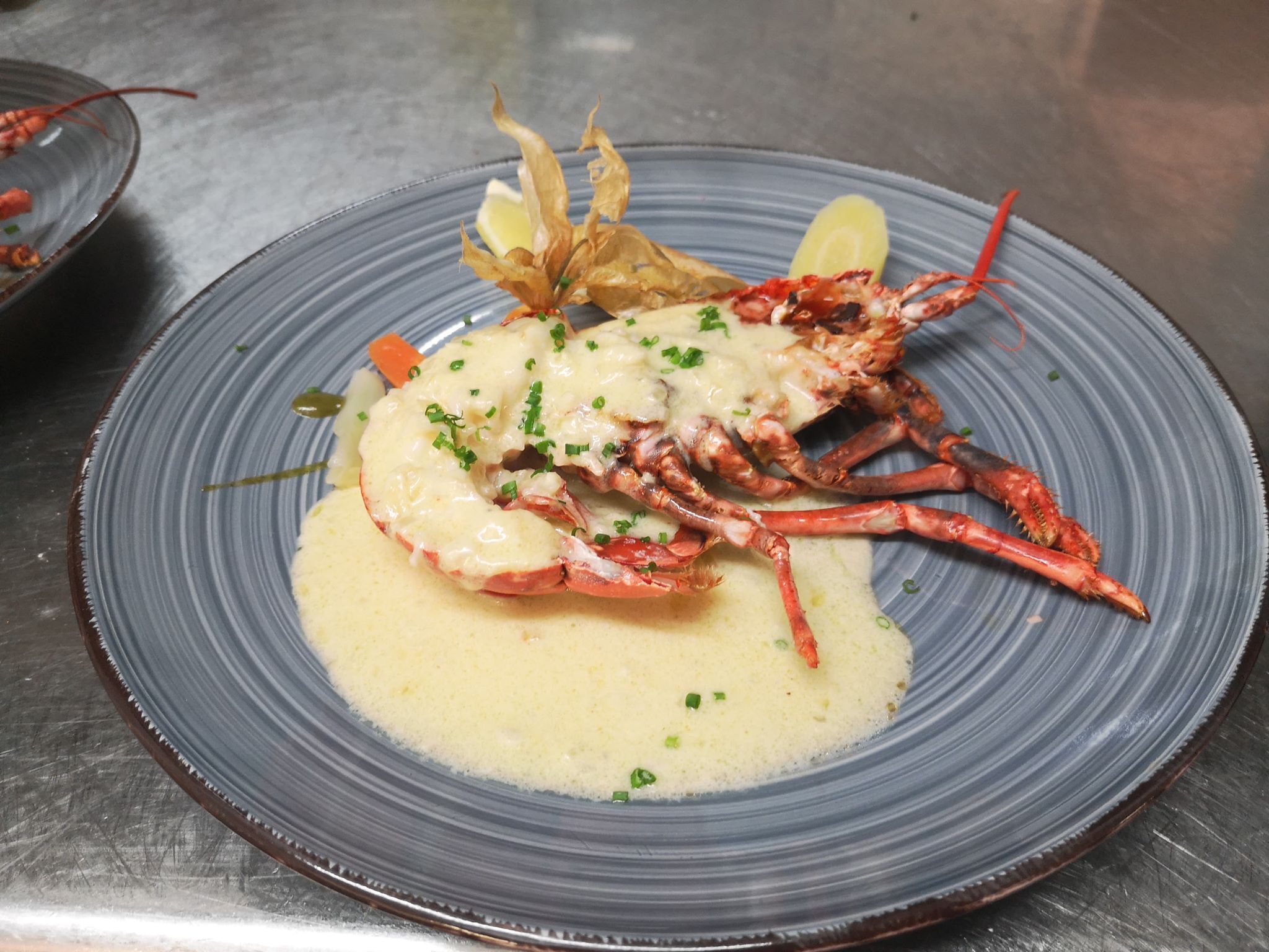 A seafood dish with a lobster tail, garnished with chives and lemon slices on a blue plate.