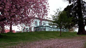 A building with a green glass conservatory, surrounded by a grassy area with cherry blossoms.