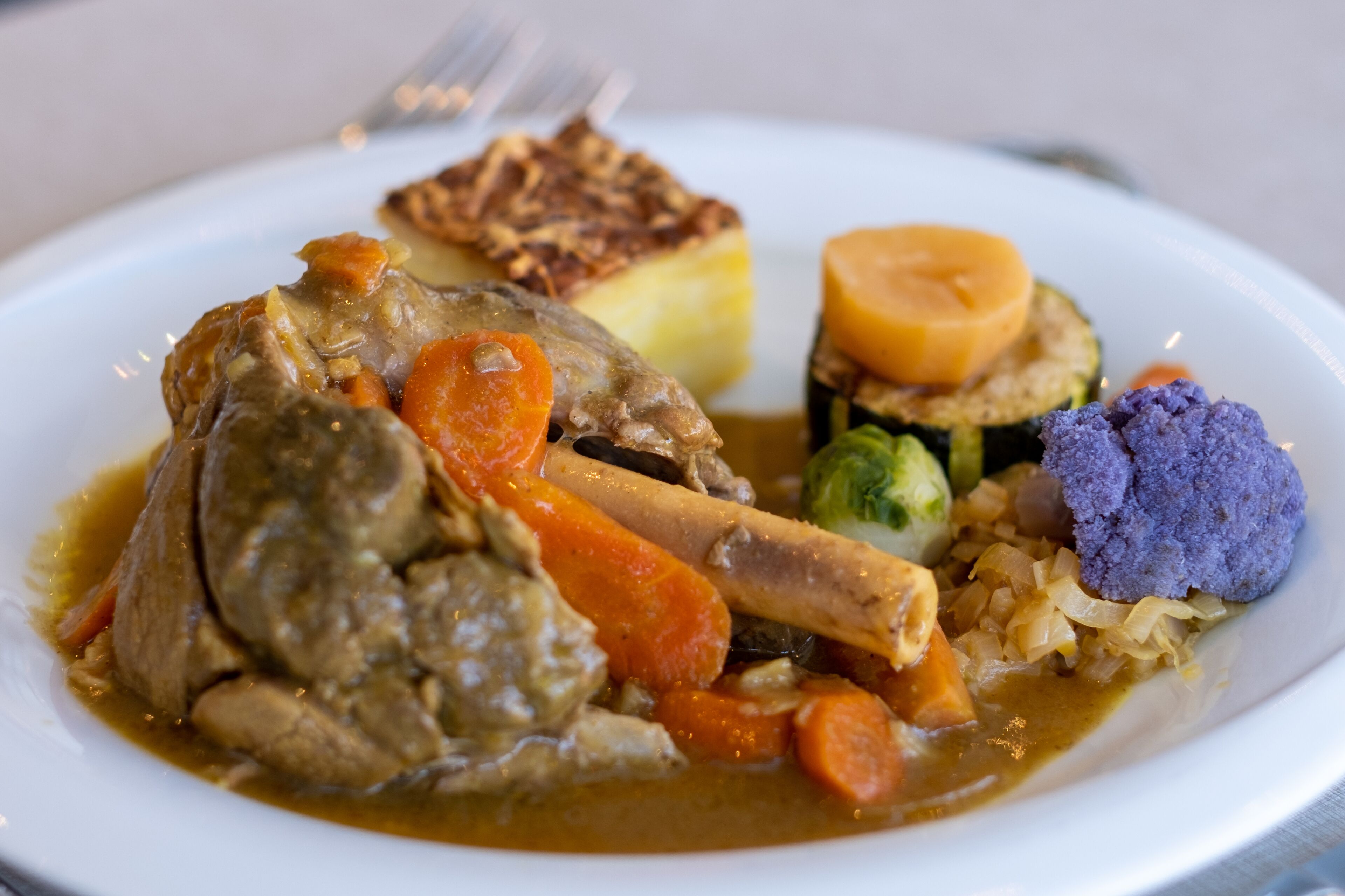 A plate of food with a piece of meat, carrots, and a side of vegetables.