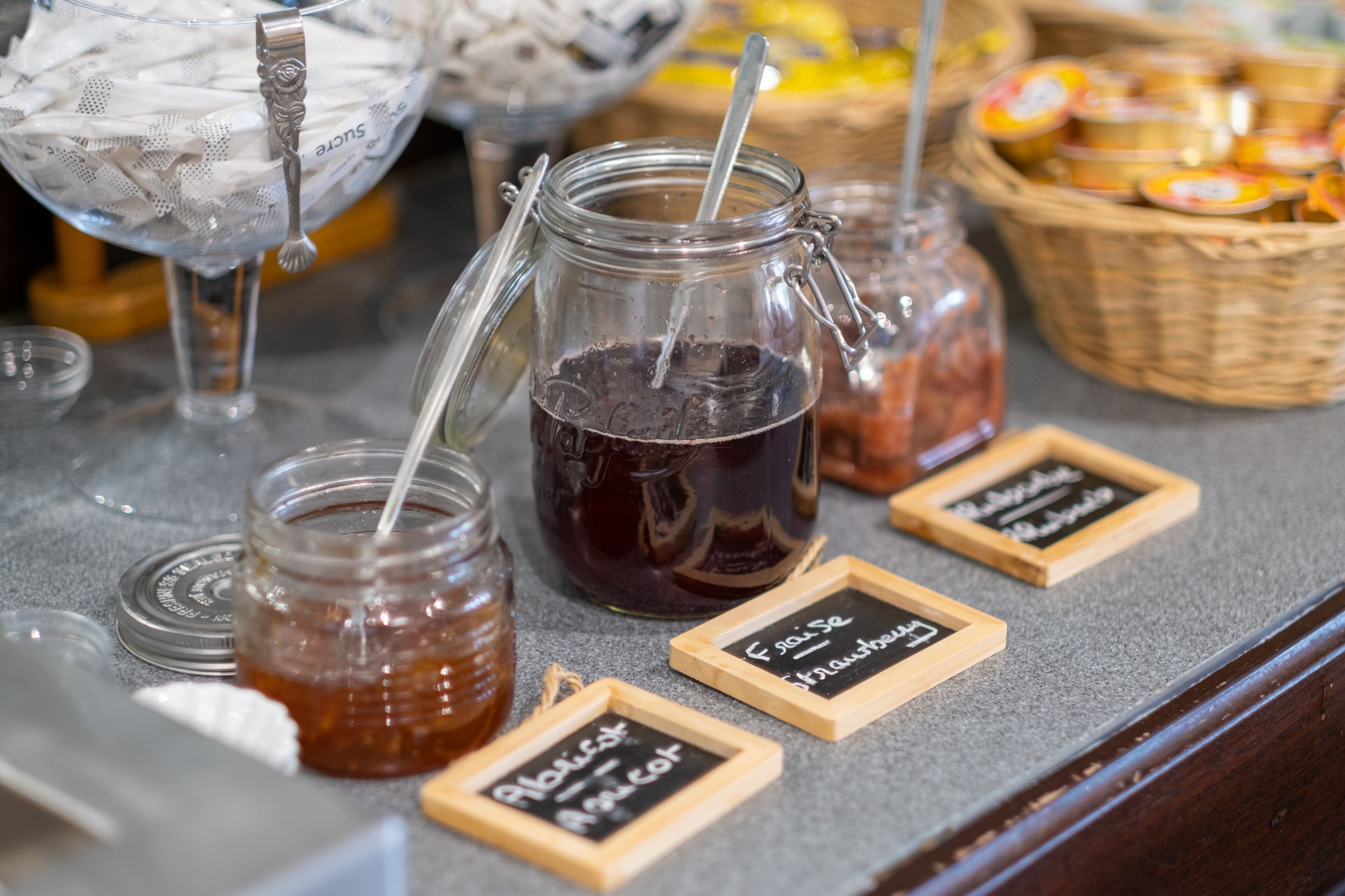 A counter with various jars of jam and honey, each labeled with their contents.