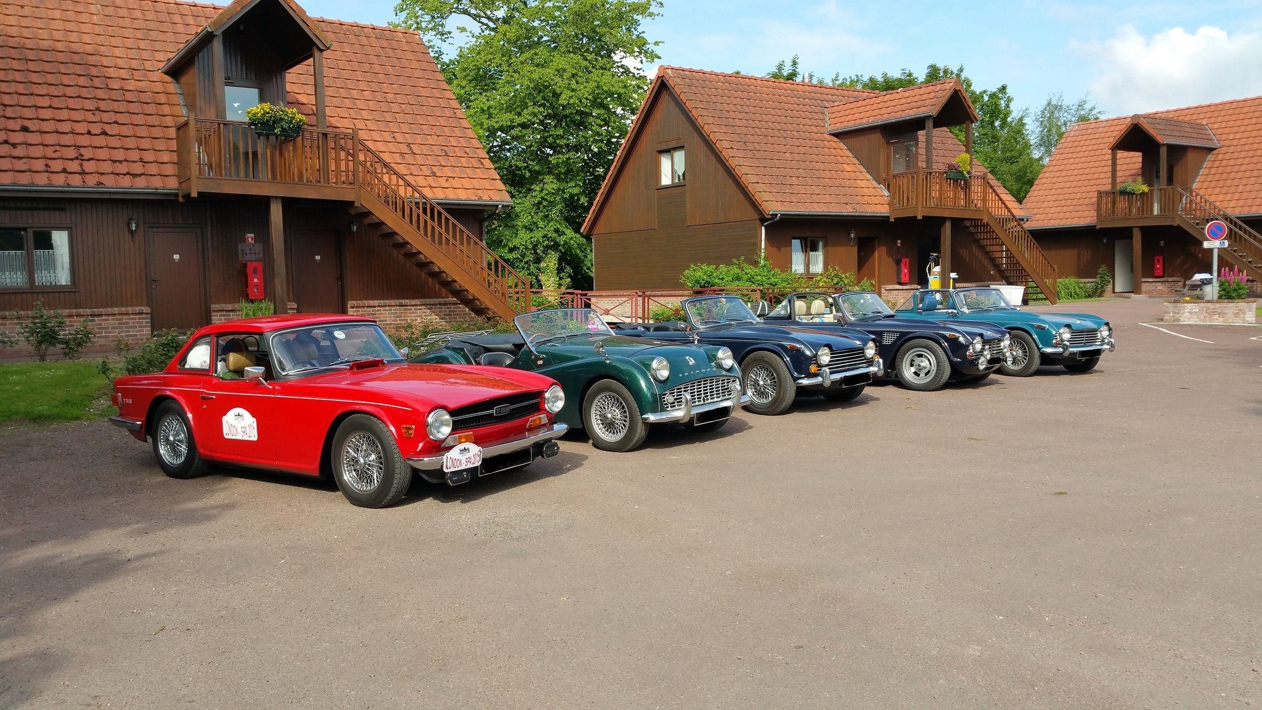 A row of vintage cars parked in front of a row of wooden cabins with balconies.