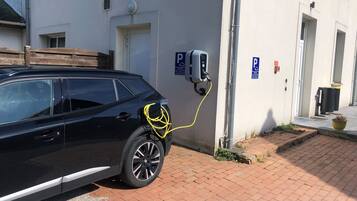 A black car parked next to a building with a charging station, a parking sign, and a trash bin.