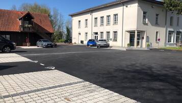 Een parkeerplaats met verschillende auto's, een gebouw met veel ramen en een dakbedekking van rode tegels.