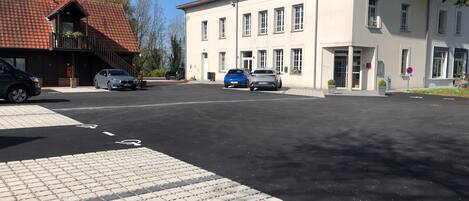 Een parkeerplaats met verschillende auto's, een gebouw met veel ramen en een dakbedekking van rode tegels.