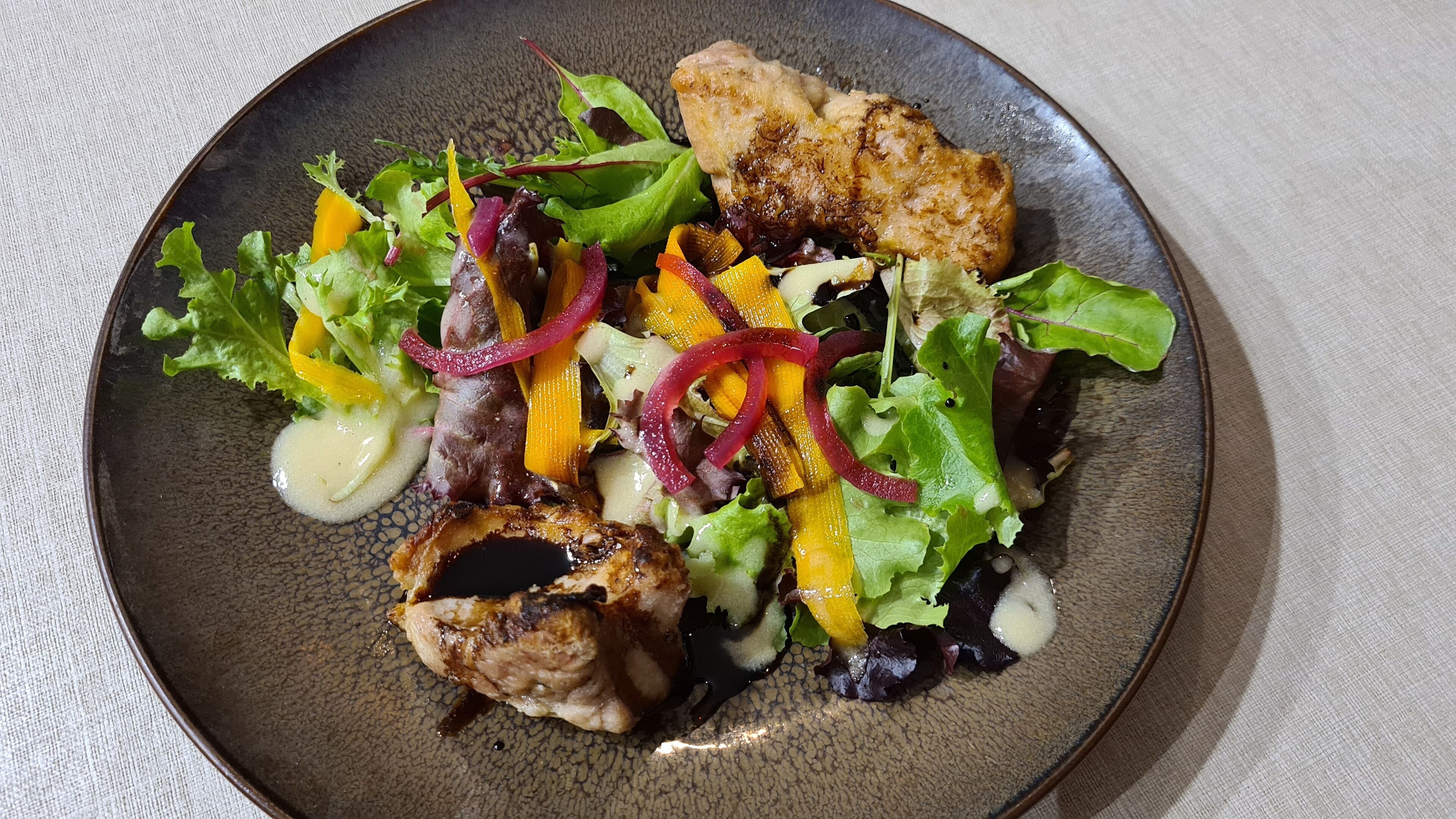 A plate of food with grilled chicken, mixed greens, and sliced vegetables.
