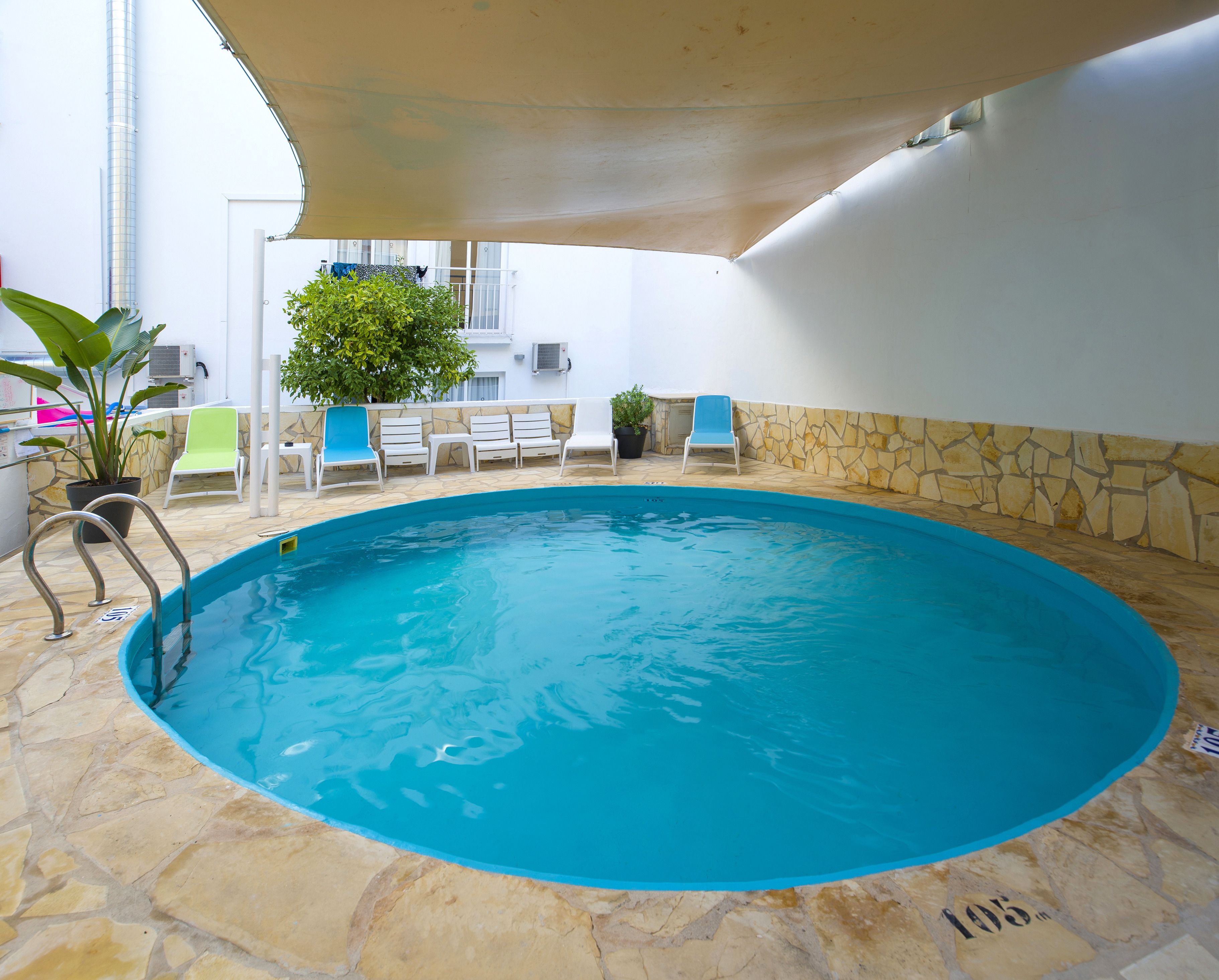 Una piscina con suelo de piedra, rodeada de sillones blancos y una planta en maceta.