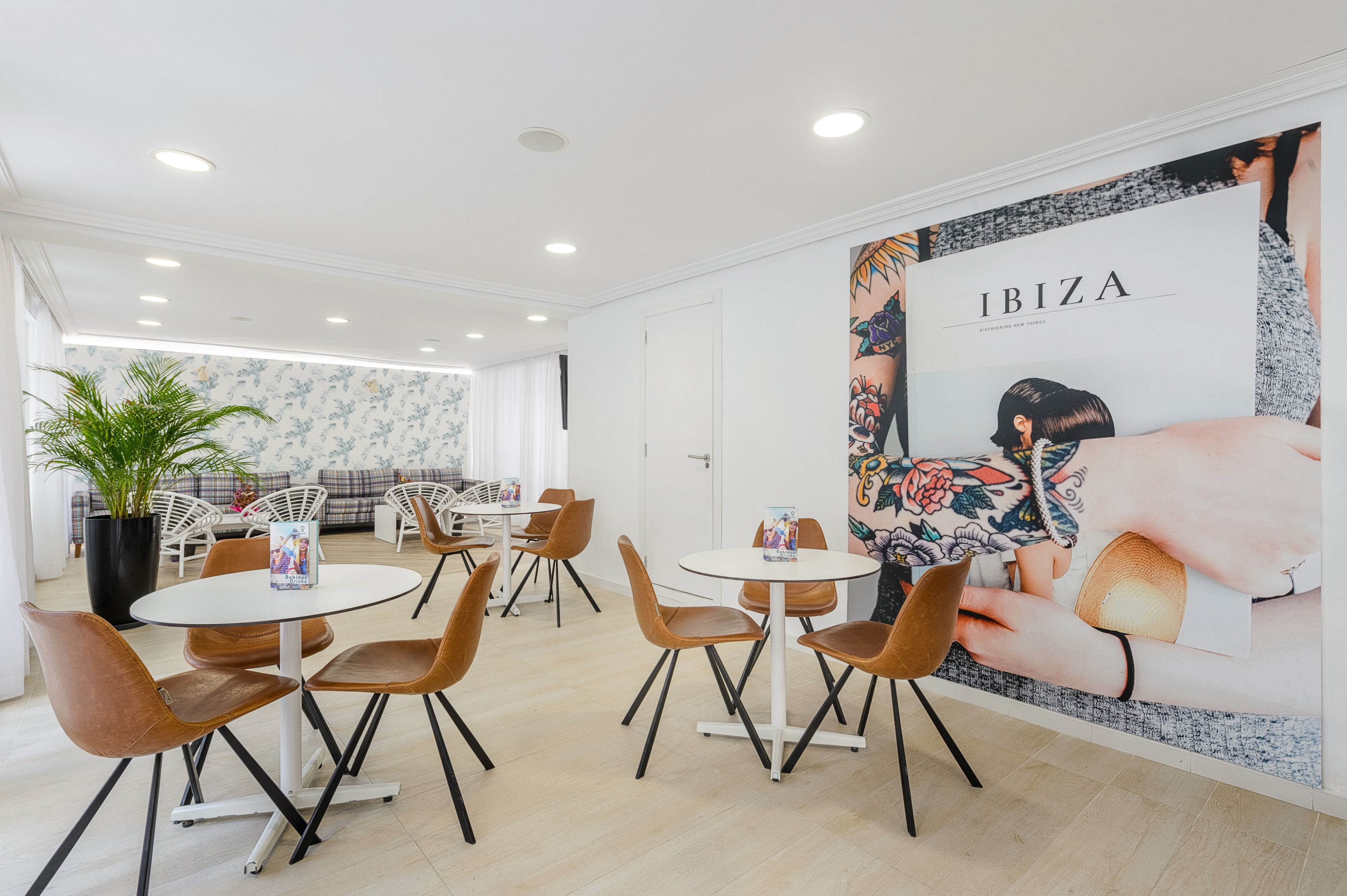 A modern lounge area with round tables and chairs, a large floral wall mural, and a potted plant.