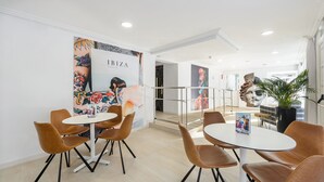 A modern hotel lobby with round tables and brown chairs, a mural on the wall, and a staircase leading to another floor. - Hotel Vibra Lei Ibiza (Ibiza Town)