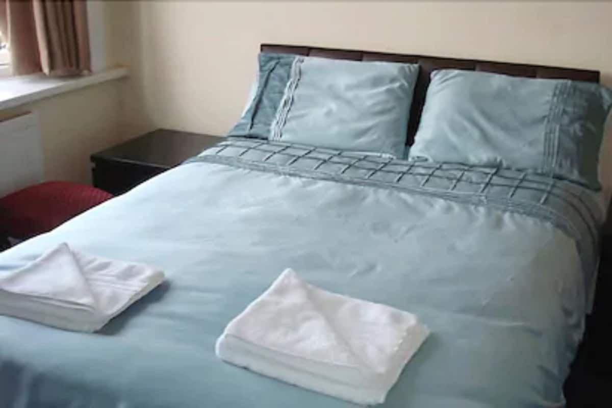 Cama bem arrumada com colcha azul, duas almofadas e uma toalha branca dobrada.