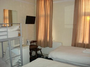 Ein Hotelzimmer mit Stockbetten, einem Schreibtisch, einem Stuhl, einem Fernseher und Vorhängen.