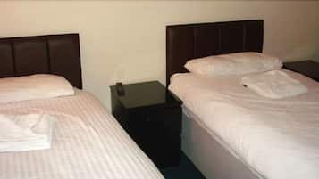 Habitación de hotel con dos camas individuales, cada una con una almohada y una toalla doblada. Hay una mesita de noche entre las camas con un teléfono y una pequeña mesa.