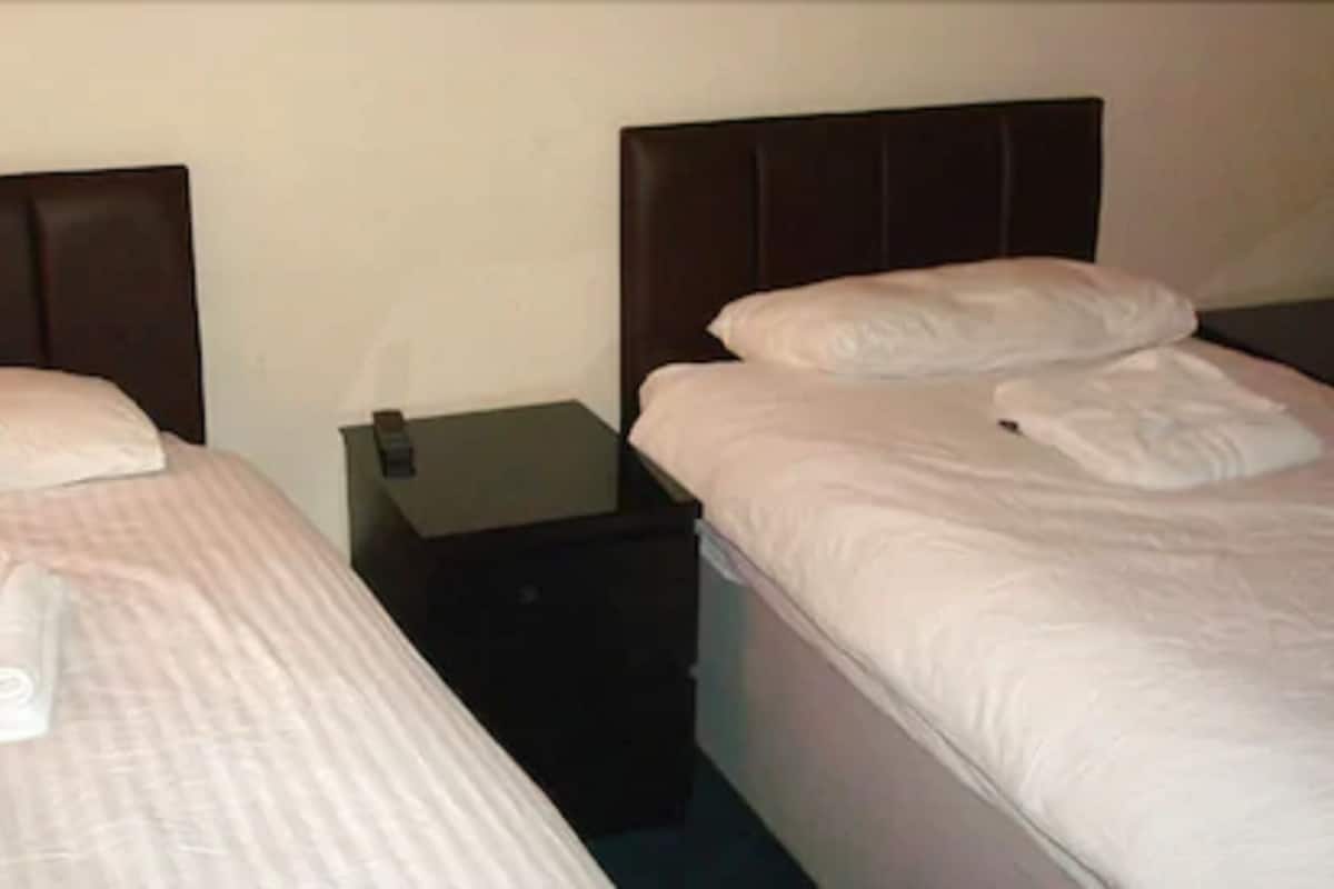Quarto de hotel com duas camas, cada uma com cabeceira, mesa de cabeceira e toalha dobrada sobre a cama.