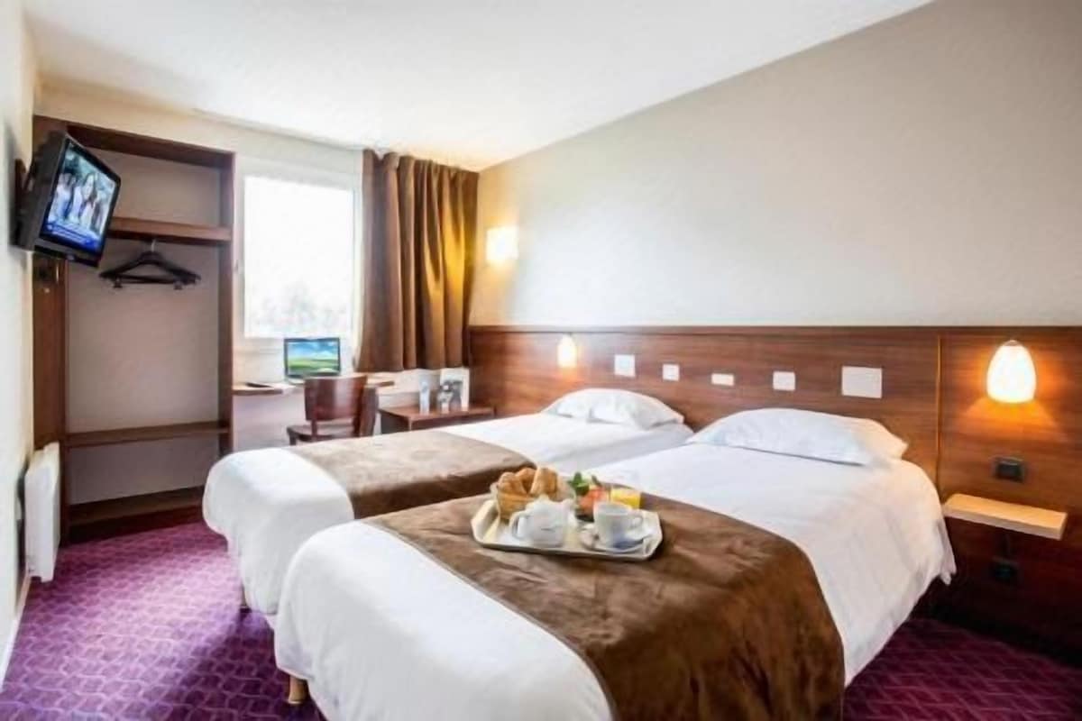 A hotel room with two beds, a desk, a TV, and a breakfast tray.