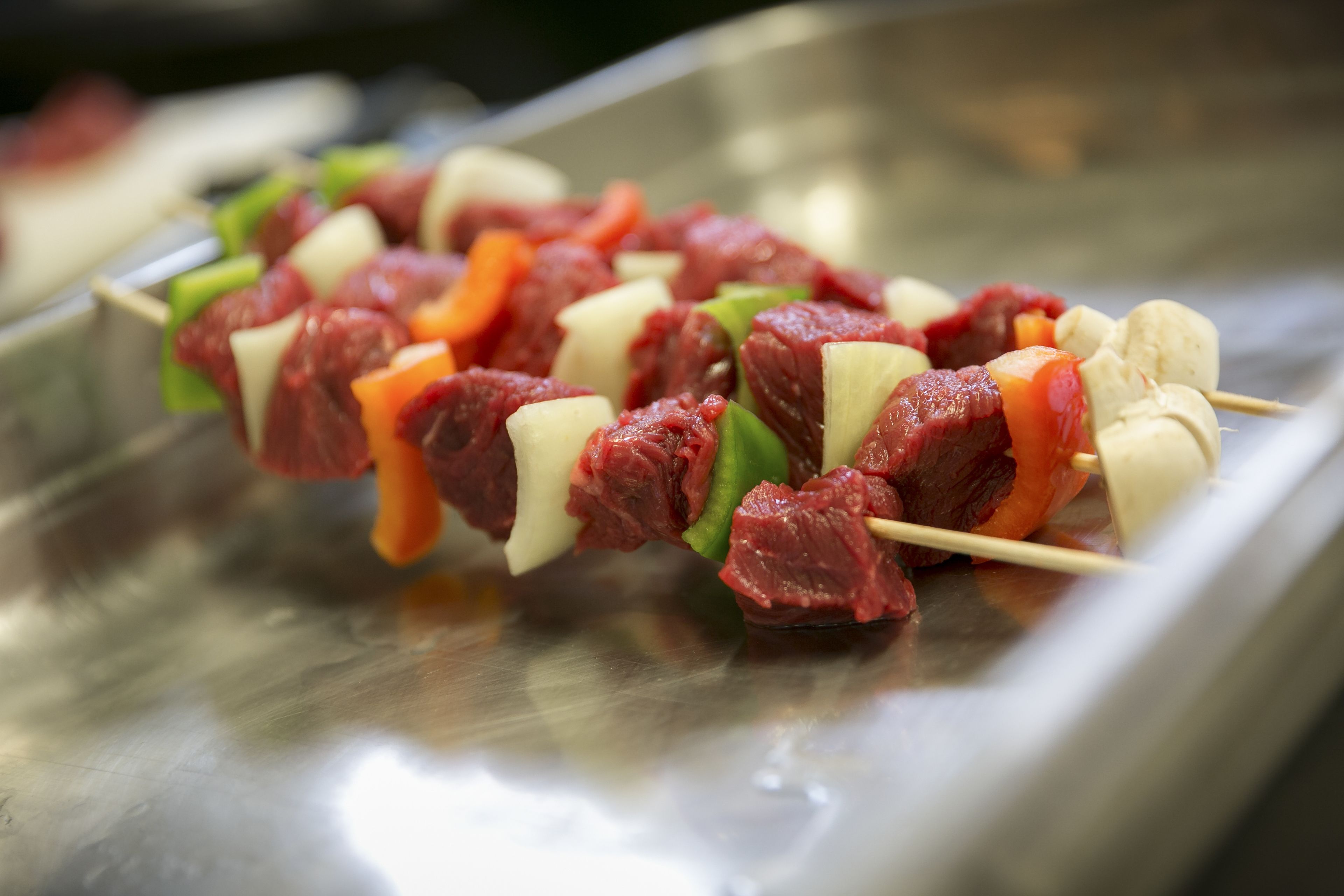 Brochetas de carne y verduras sobre una bandeja de acero inoxidable.