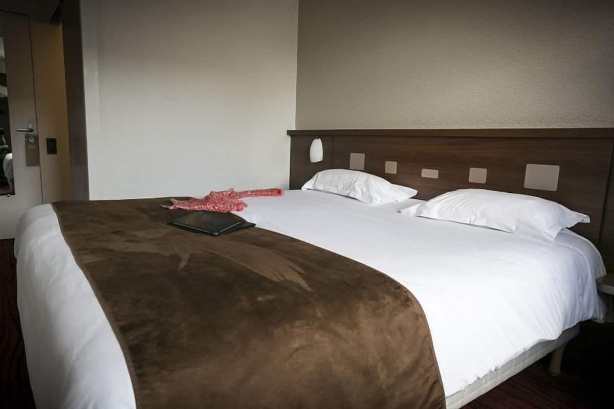 A hotel room with a large bed, a brown accent pillow, and a white headboard.