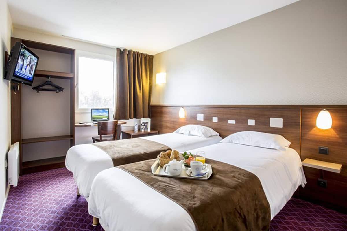 A hotel room with two beds, a desk, a TV, and a breakfast tray on the bed.