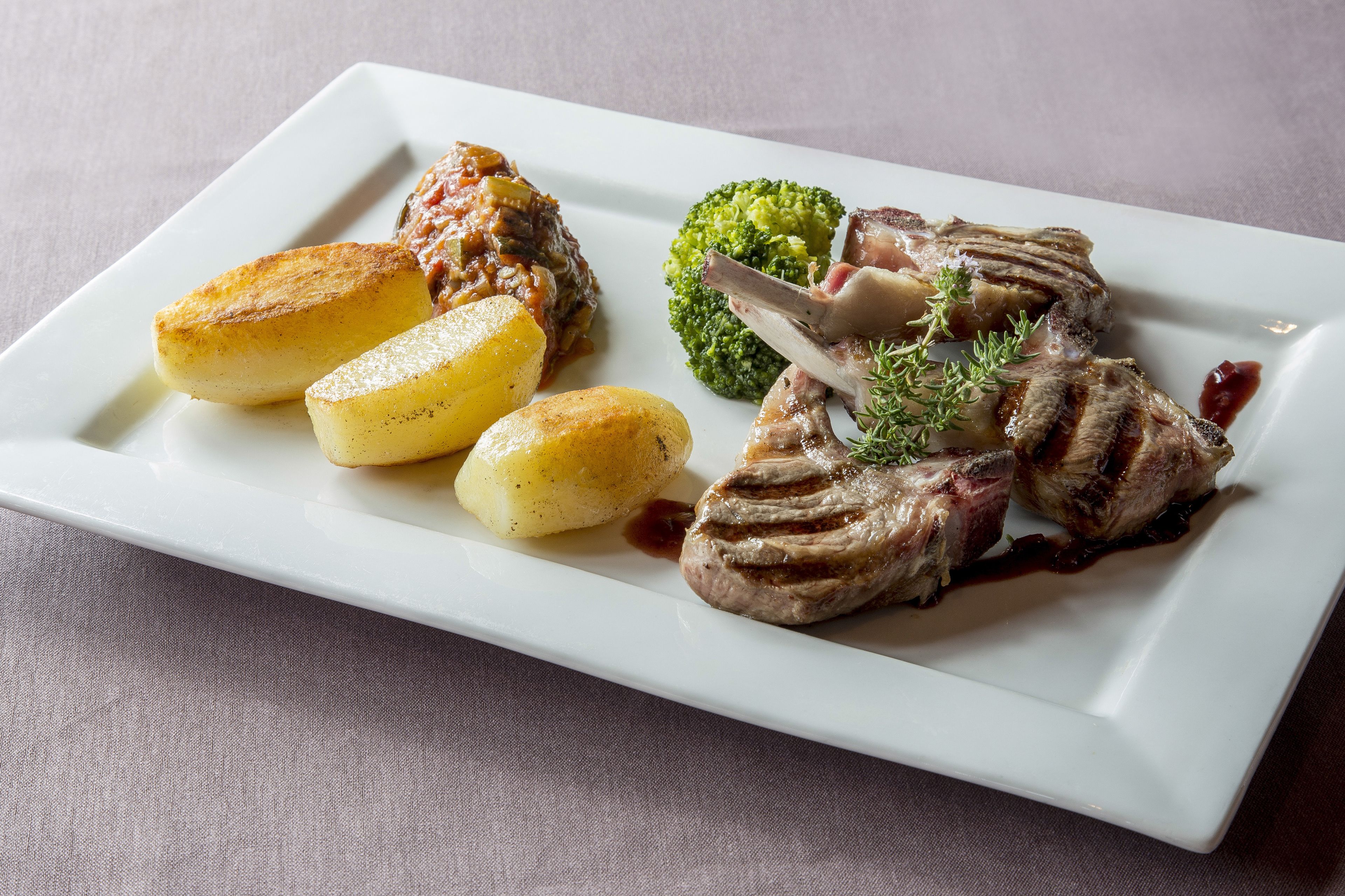Un plato rectangular blanco con un bistec, papas asadas y brócoli.