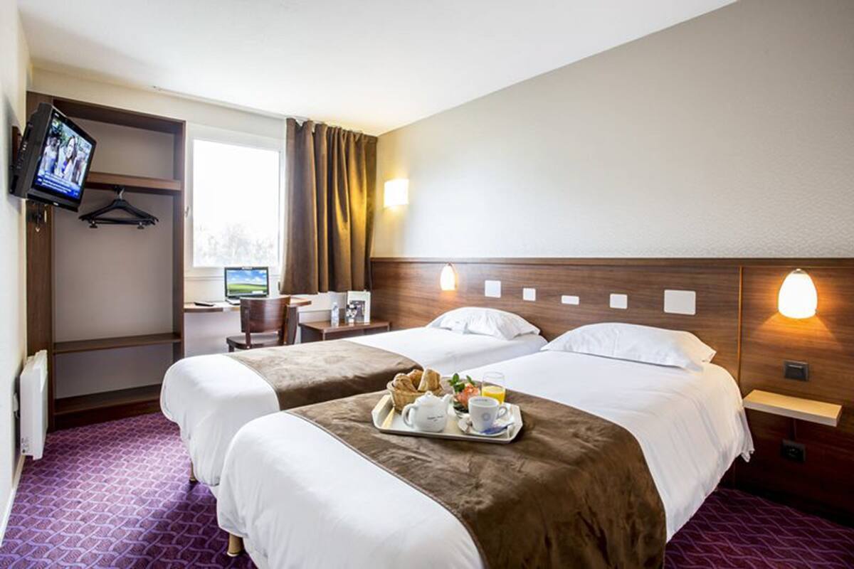 A hotel room with two beds, a desk, a TV, and a breakfast tray.