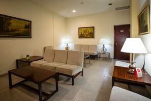 Habitación de hotel con sofá, dos sillones, una mesita de centro de madera, una mesita auxiliar y una lámpara.