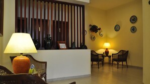 Un área de recepción con mostrador, dos sillas de mimbre, una mesa y una lámpara.
