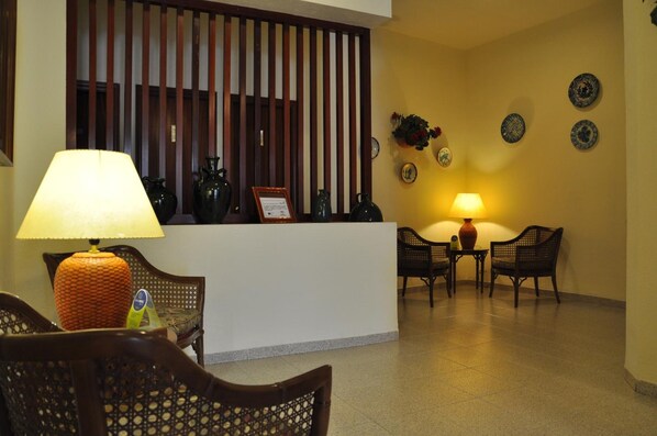 Un área de recepción con mostrador, dos sillas de mimbre, una mesa y una lámpara.