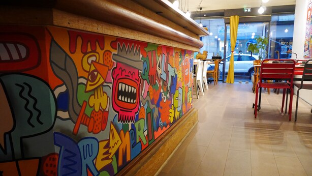 A colorful mural with abstract and cartoonish designs on a wall in a public space. - Street Art Hotel (Rouen)