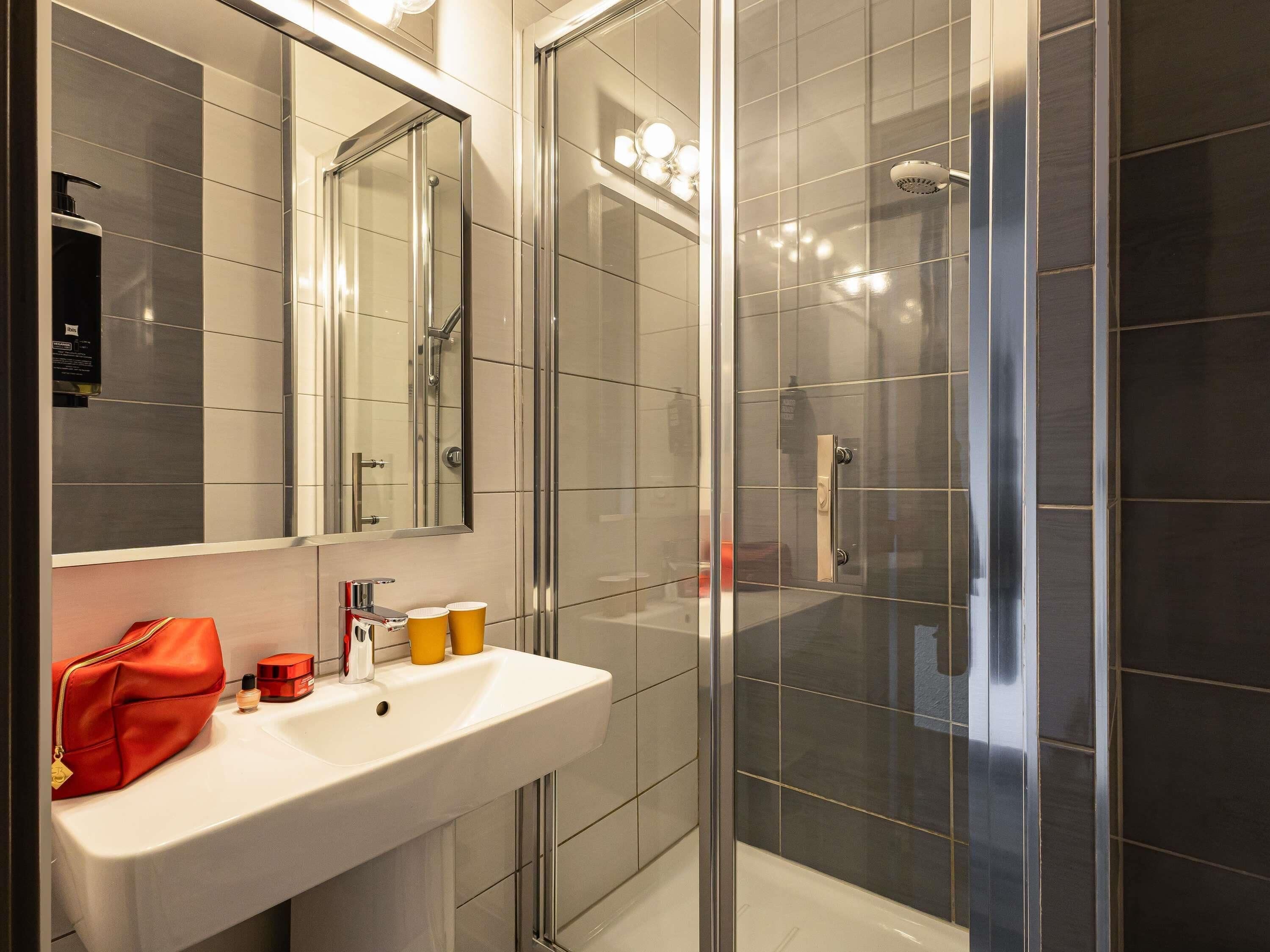 Un baño moderno con cabina de ducha de vidrio, un lavamanos blanco con artículos de aseo y un espejo grande.