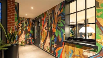 A hallway with a colorful abstract mural on the walls, a potted plant, and a window with a view of the interior.