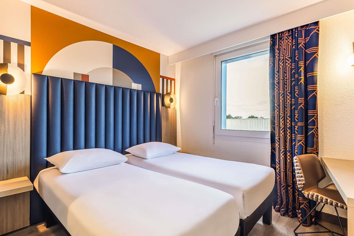 A hotel room with two beds, a desk, and a chair.