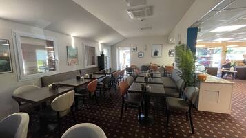 Een restaurant met zitjes en tafels, een kamerbreed tapijt met patroon en lijstjes met foto’s aan de muur.