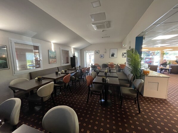 A restaurant with booths and tables, a patterned carpet, and framed pictures on the walls.
