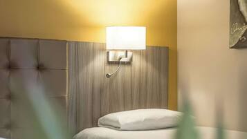 A hotel room with a bed, a bedside table, and a wall-mounted lamp.