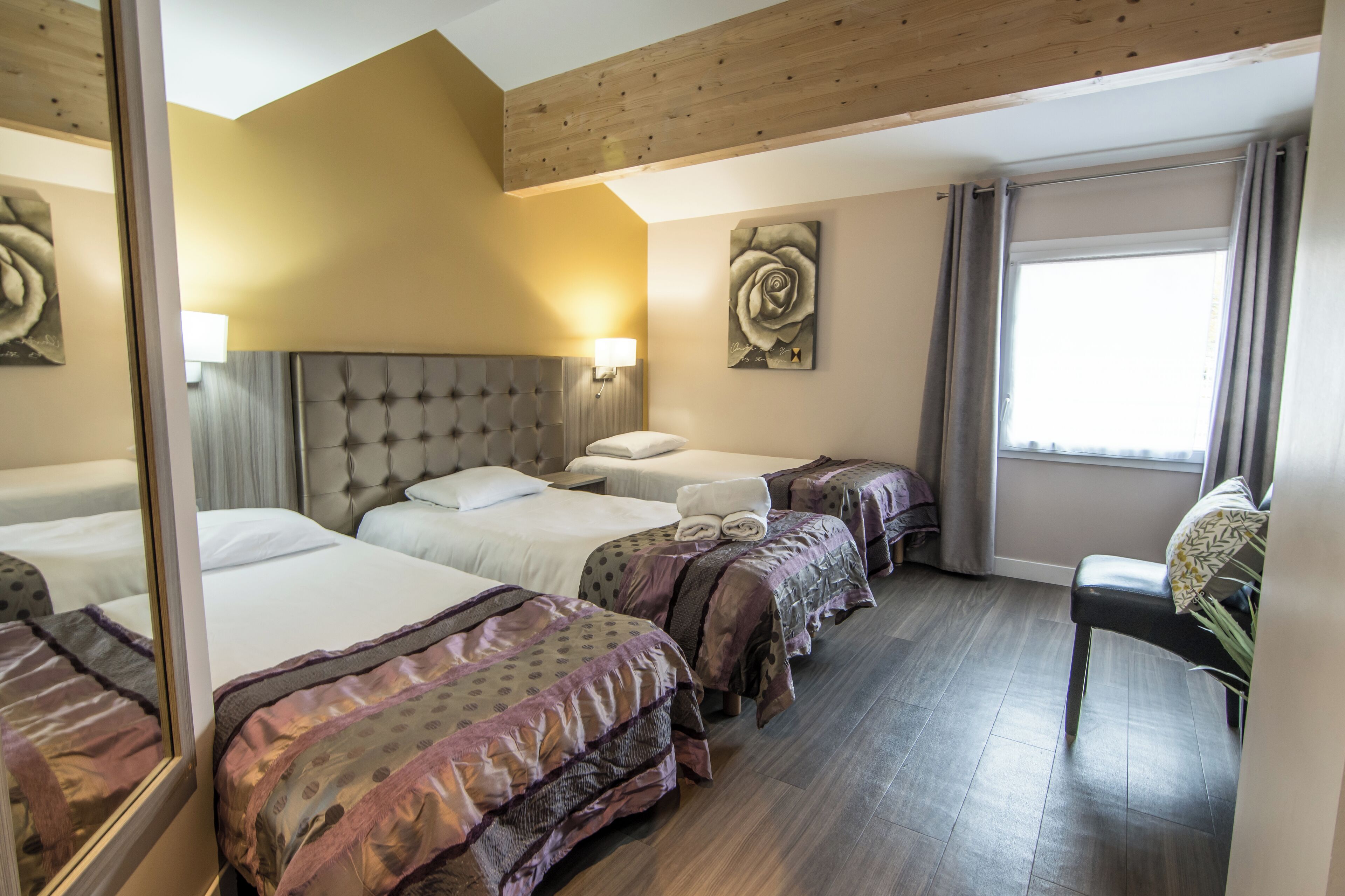 Ett hotellrum med tre sängar, en stor spegel, ett träpanelat tak och ett fönster med gardiner.