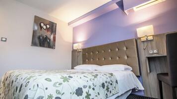 A hotel room with a tufted headboard, a floral bedspread, a painting on the wall, and two wall-mounted lamps.