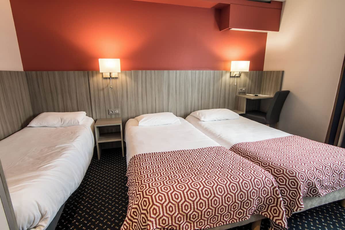 A hotel room with two single beds, a small desk, a chair, and a nightstand.