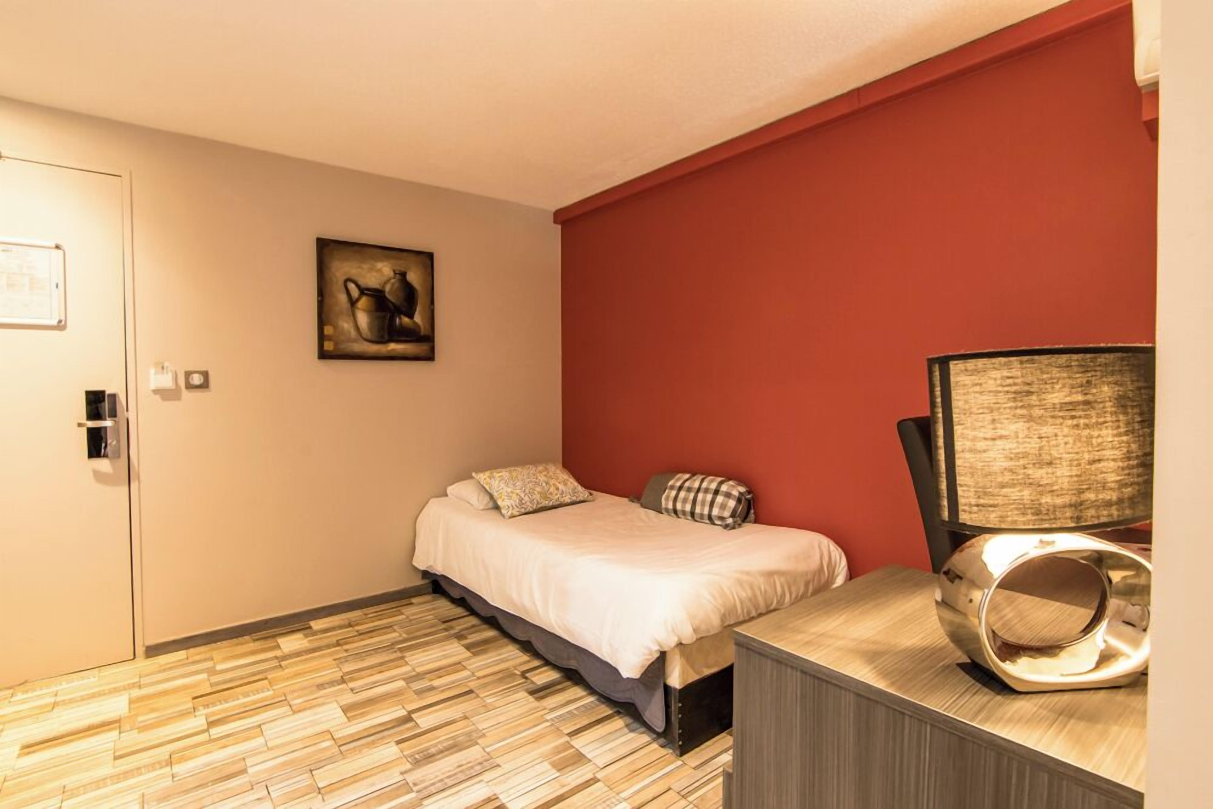 A bedroom with a bed, a desk, a chair, a lamp, and a painting on the wall.