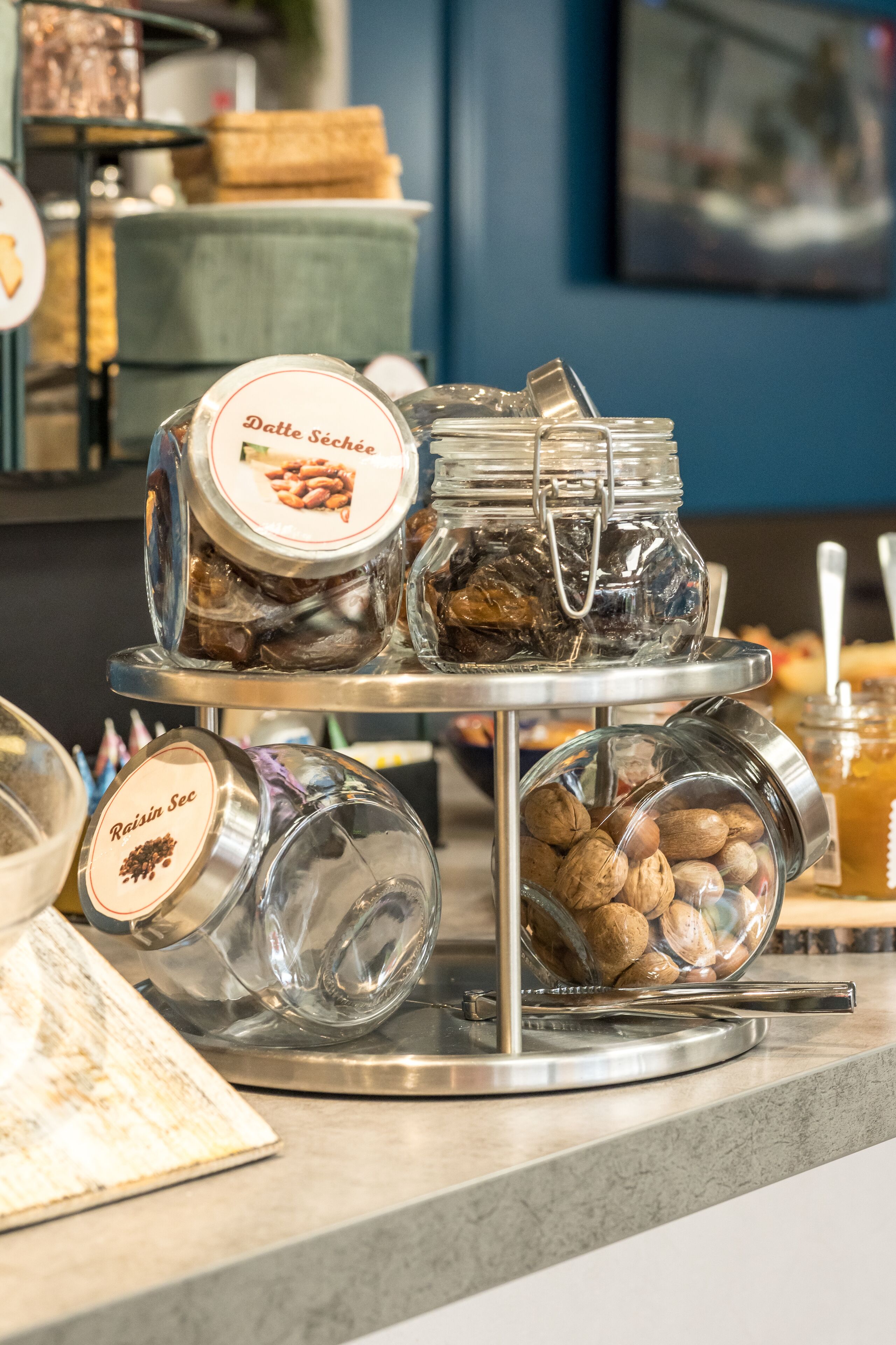 A display of glass jars containing various nuts and seeds, arranged on a metal stand.