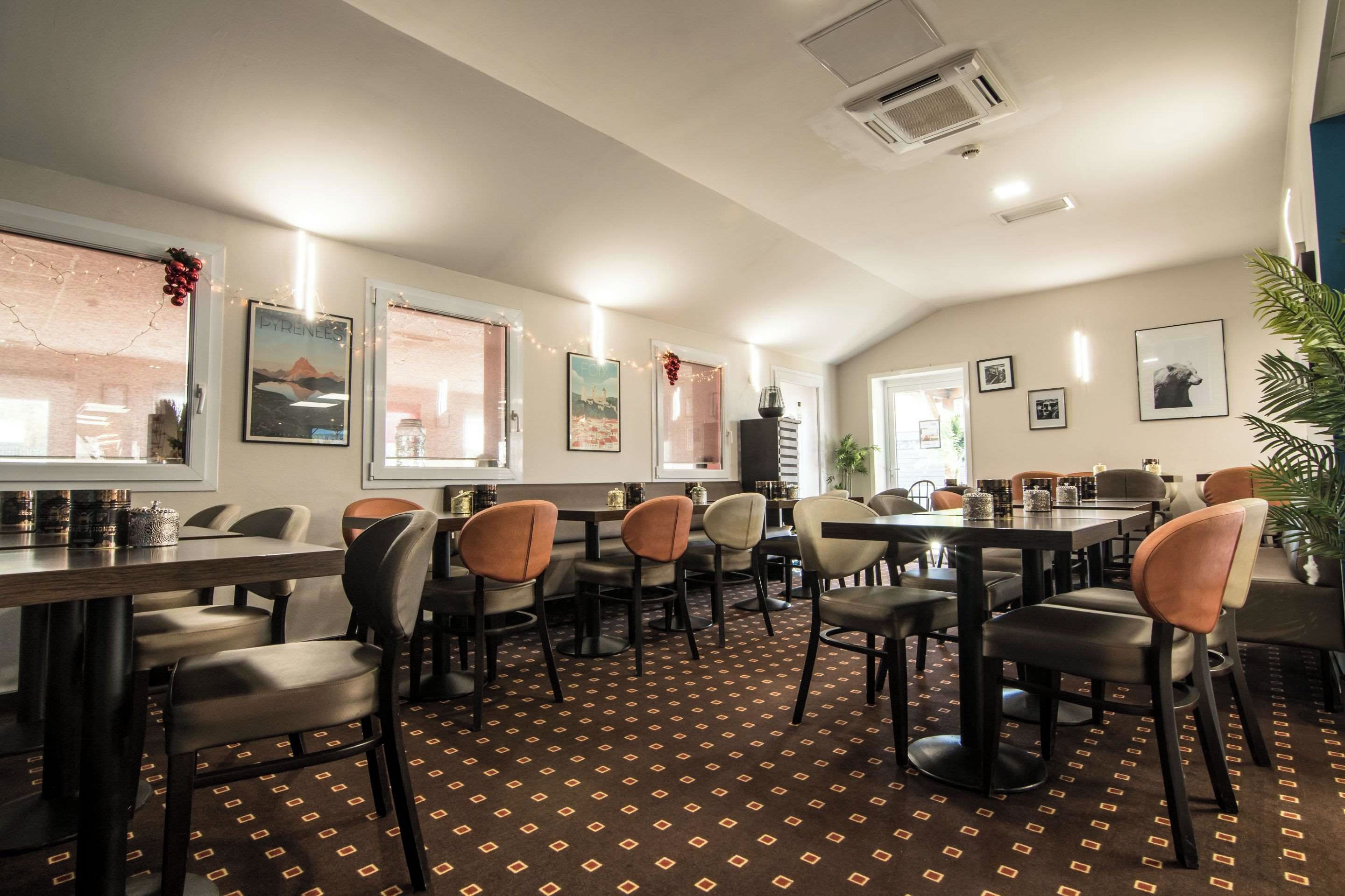 A restaurant with multiple tables and chairs, a patterned carpet, and framed pictures on the walls.