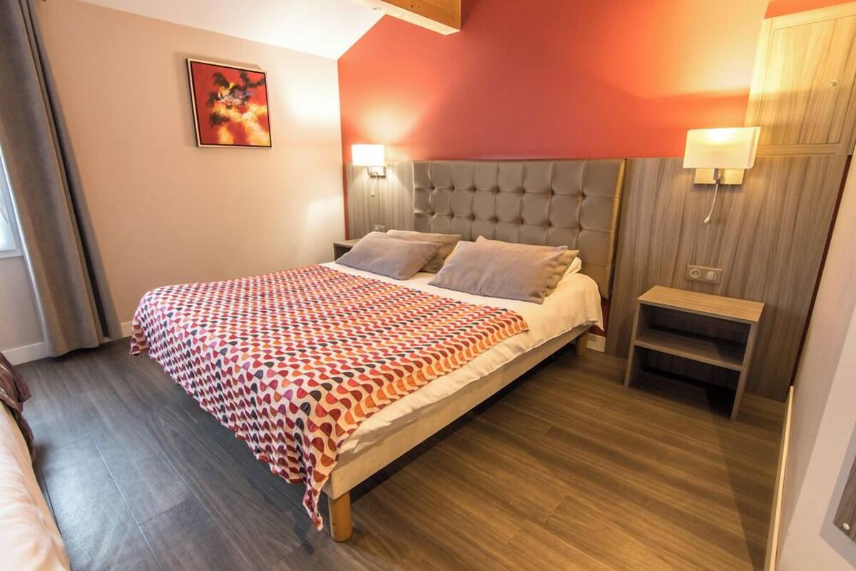 A hotel room with a large bed, a wooden nightstand, and a wall-mounted lamp.