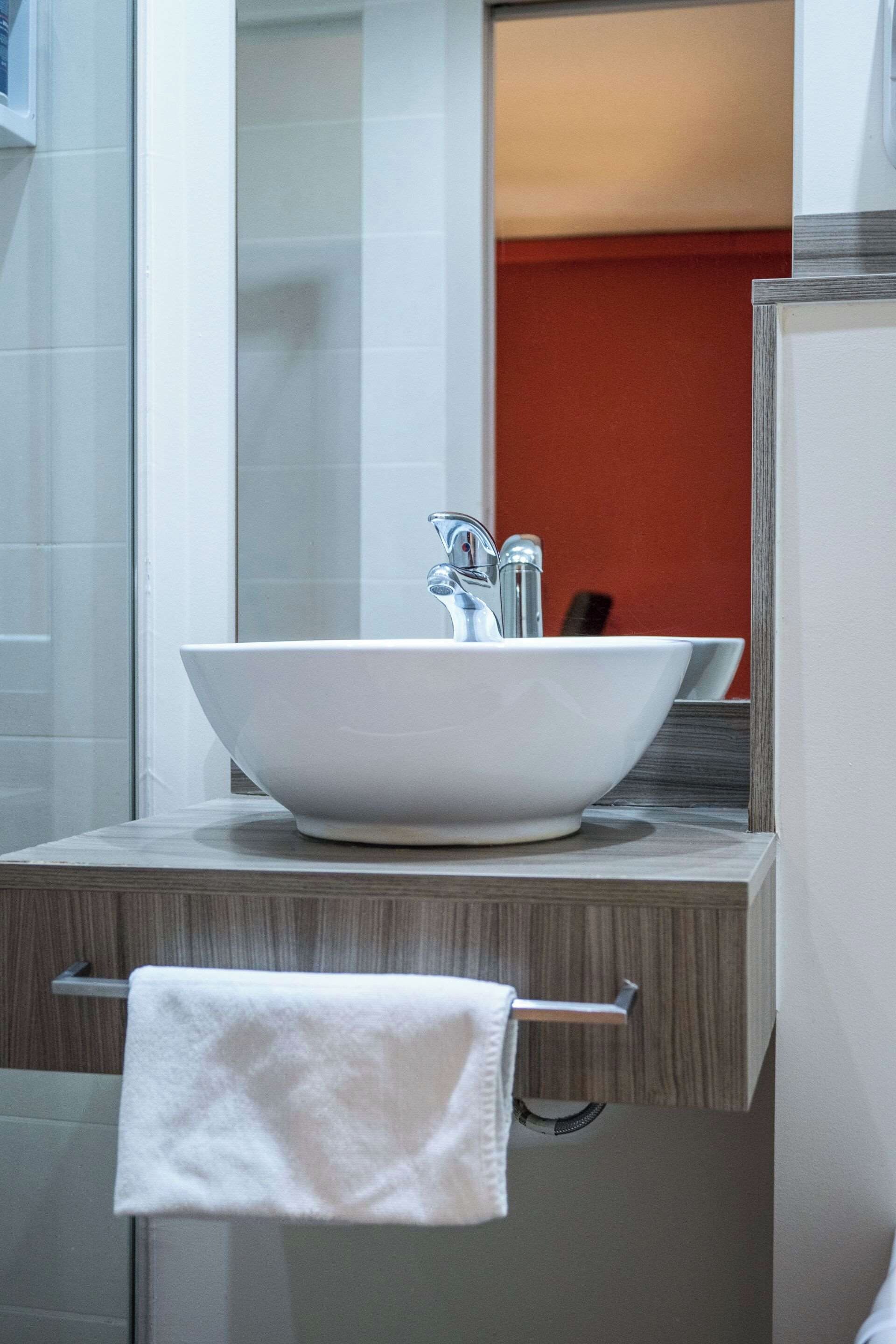 A bathroom with a large white vessel sink, a towel hanging on a rack, and a mirror above the sink.