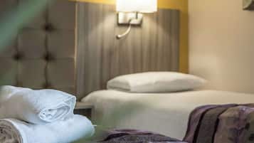 Une chambre d’hôtel avec deux lits, une lampe fixée au mur et une plante au premier plan.