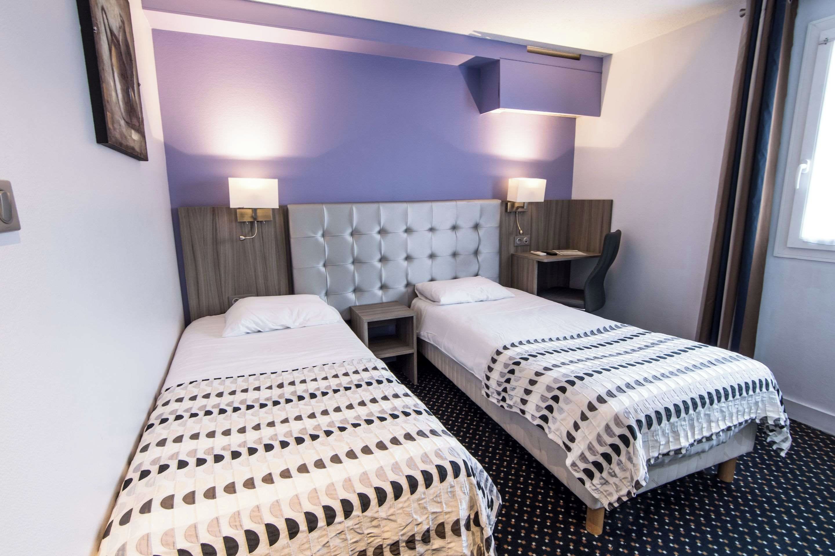 Een hotelkamer met twee enkele bedden, een klein bureau en een stoel.