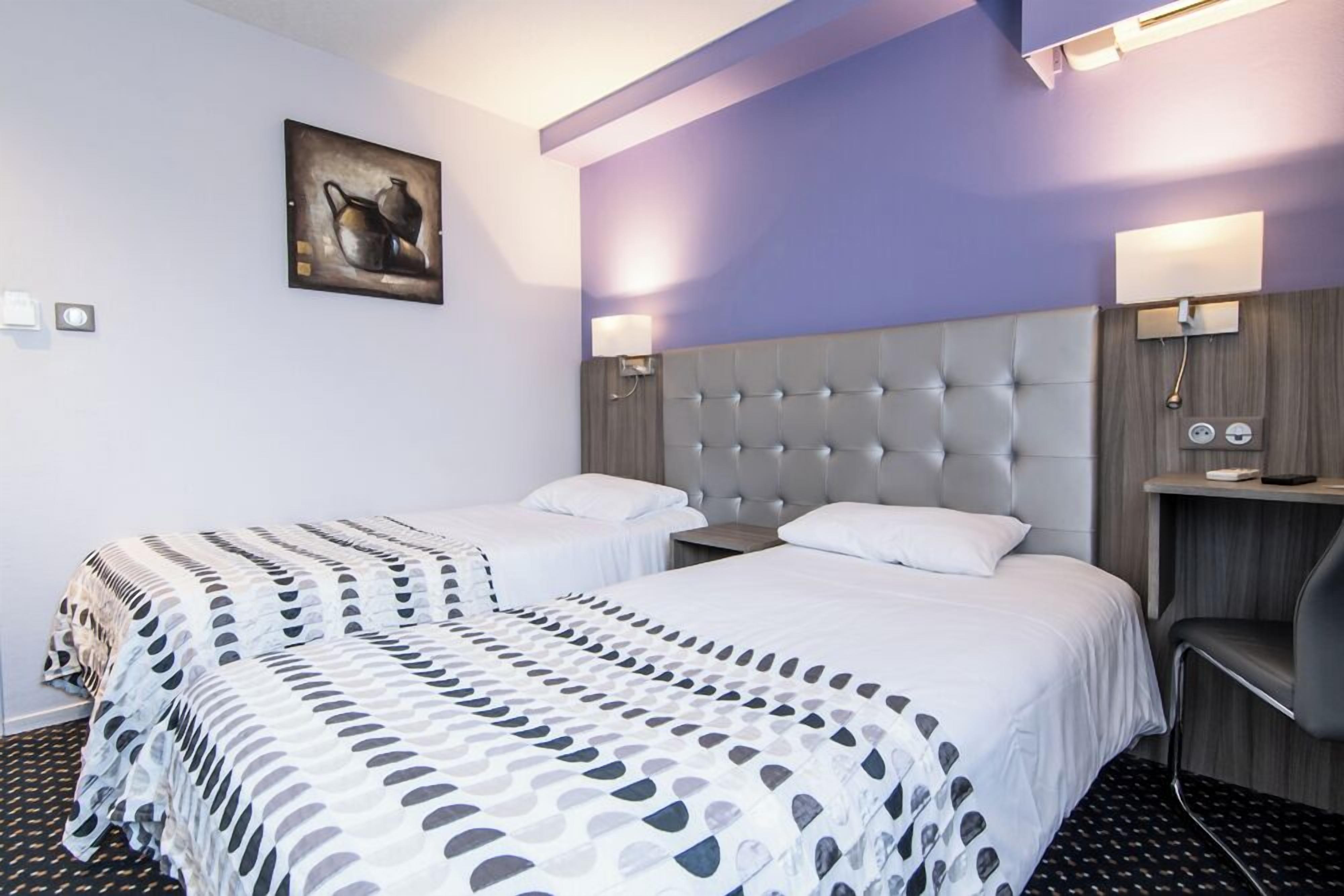Habitación de hotel con dos camas, un cabecero grande, lámparas de noche, un cuadro en la pared y una silla.