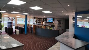 A modern bar area with seating, a counter, and a television screen. - Brit Hotel Confort Foix (Foix)
