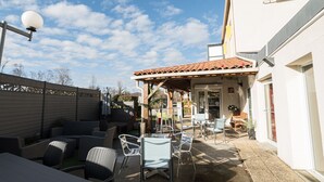 An outdoor patio area with wicker furniture, a pergola, and a view of the adjacent building. - Brit Hotel Confort Foix (Foix)