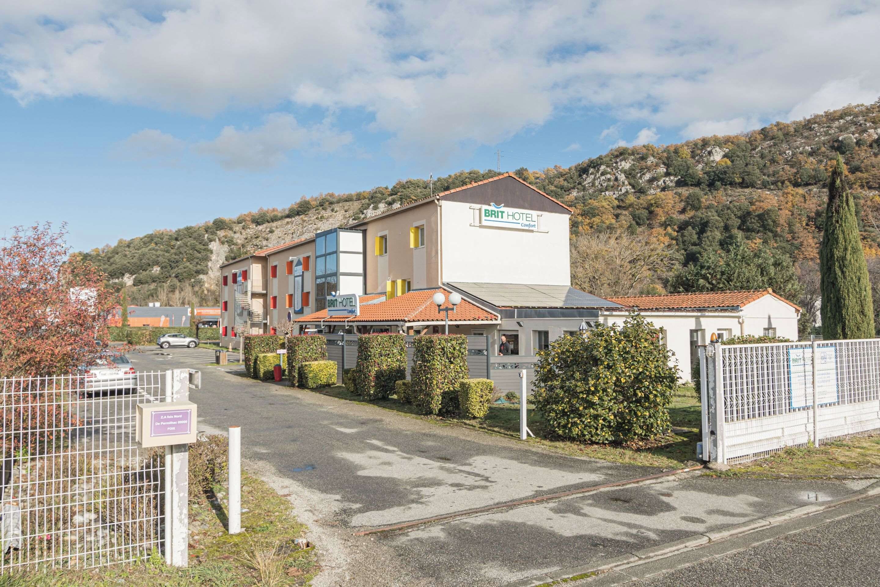 Et hotel med et skilt, der viser 'BRIT HOTEL Comfort', og en parkeringsplads foran.
