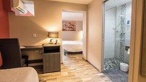 A hotel room with a bed, desk, chair, and a shower area. - Brit Hotel Confort Foix (Foix)