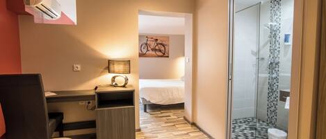 Habitación de hotel con cama, escritorio, silla y zona de ducha.