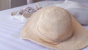 Una cama con un sombrero de paja y pantuflas, una puerta al fondo y una persona en movimiento.